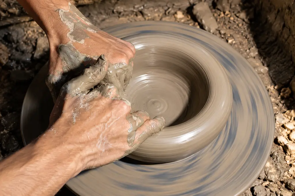 Hands opening a spinning ring of grey clay on the wheel, the motion blurred.